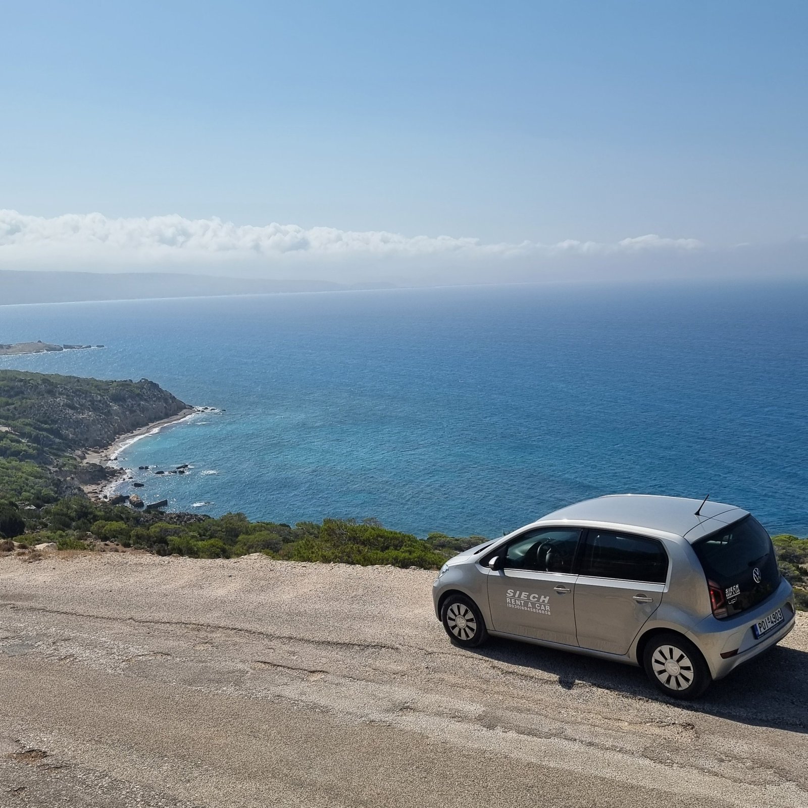 Silver local rental car parked on a coastal viewpoint above the blue sea in Rhodes, photographed by Looneytravels.