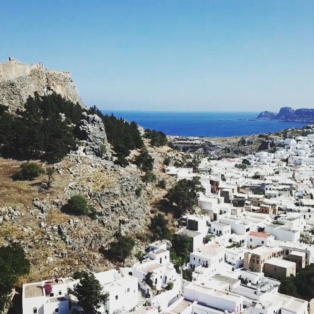 Panoramic view of white houses in Lindos village below the historic Acropolis on Rhodes Island, Greece.