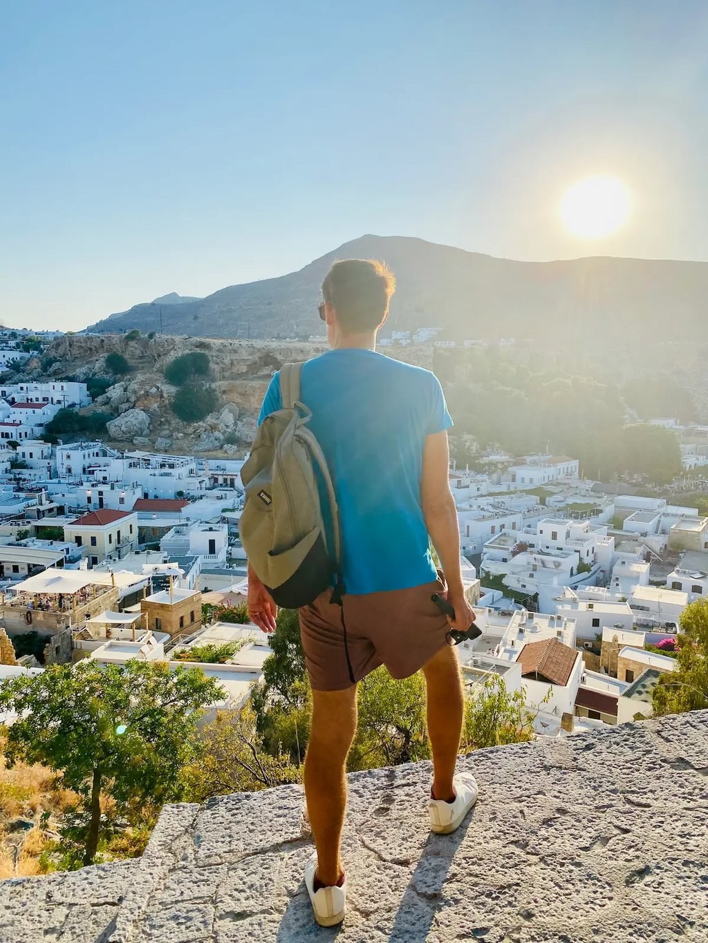 A traveller with a backpack looking over a hillside town in Rhodes at sunset
