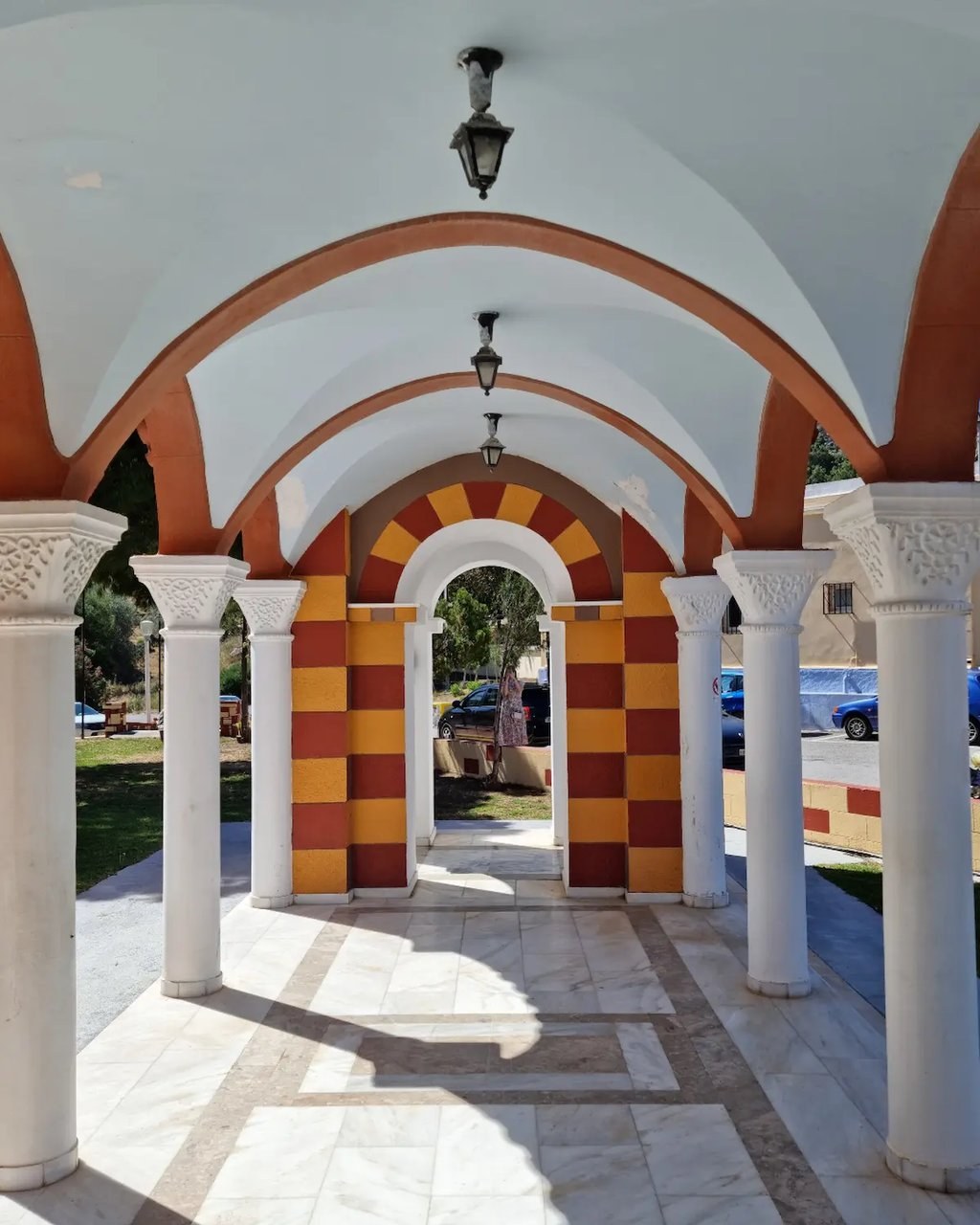 White marble colonnade with arched ceilings and striped stone pillars in a Mediterranean courtyard.